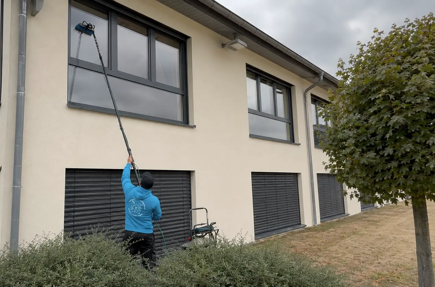 Mitarbeiter reinigt Fenster eines Gewerbeobjekts mit Teleskopstange in Bamberg