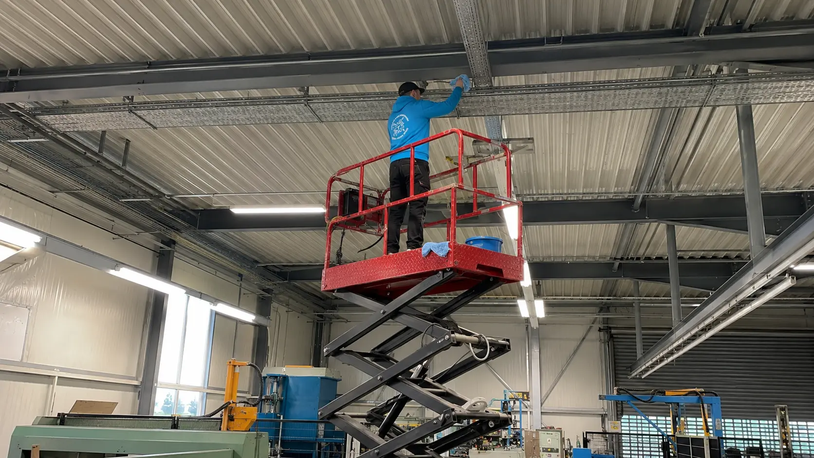 Mitarbeiter reinigt Deckenbereiche in einer Industriehalle auf einer Scherenbühne in Bamberg